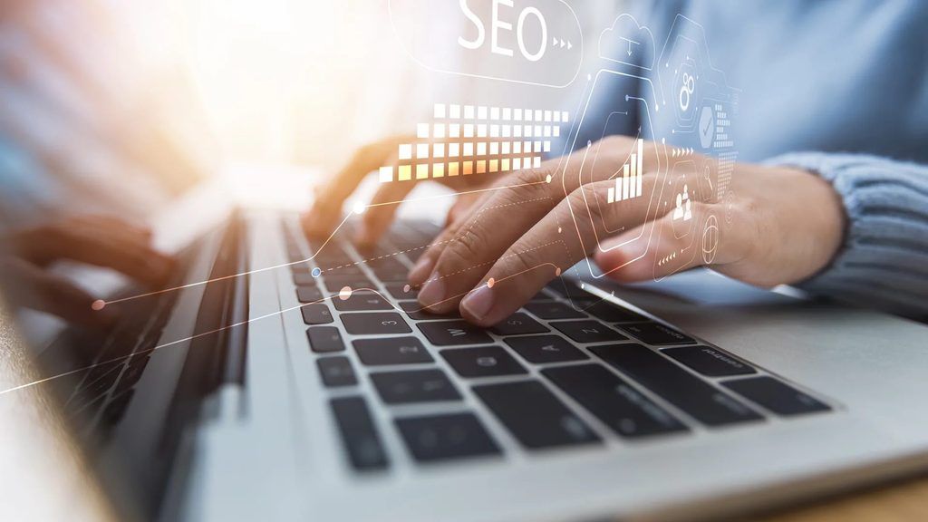 Estrategia De Seo Gestionada Por Una Agencia De Marketing O Ia: Persona Trabajando En Un Portátil Con Iconografía De Seo Y Marketing Digital Superpuesta